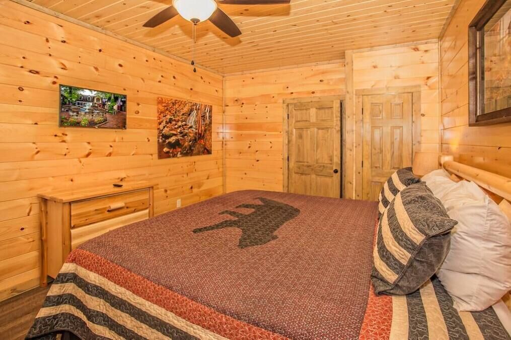 Camera da letto in un cottage di legno con un letto, un comodino, una ventola a soffitto e una porta.