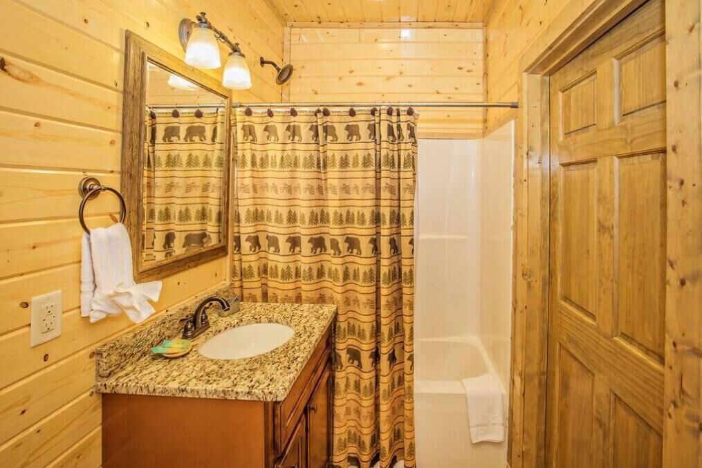 A wooden cabin bathroom with a granite sink, a mirror, a towel rack, and a shower curtain with a bear pattern.