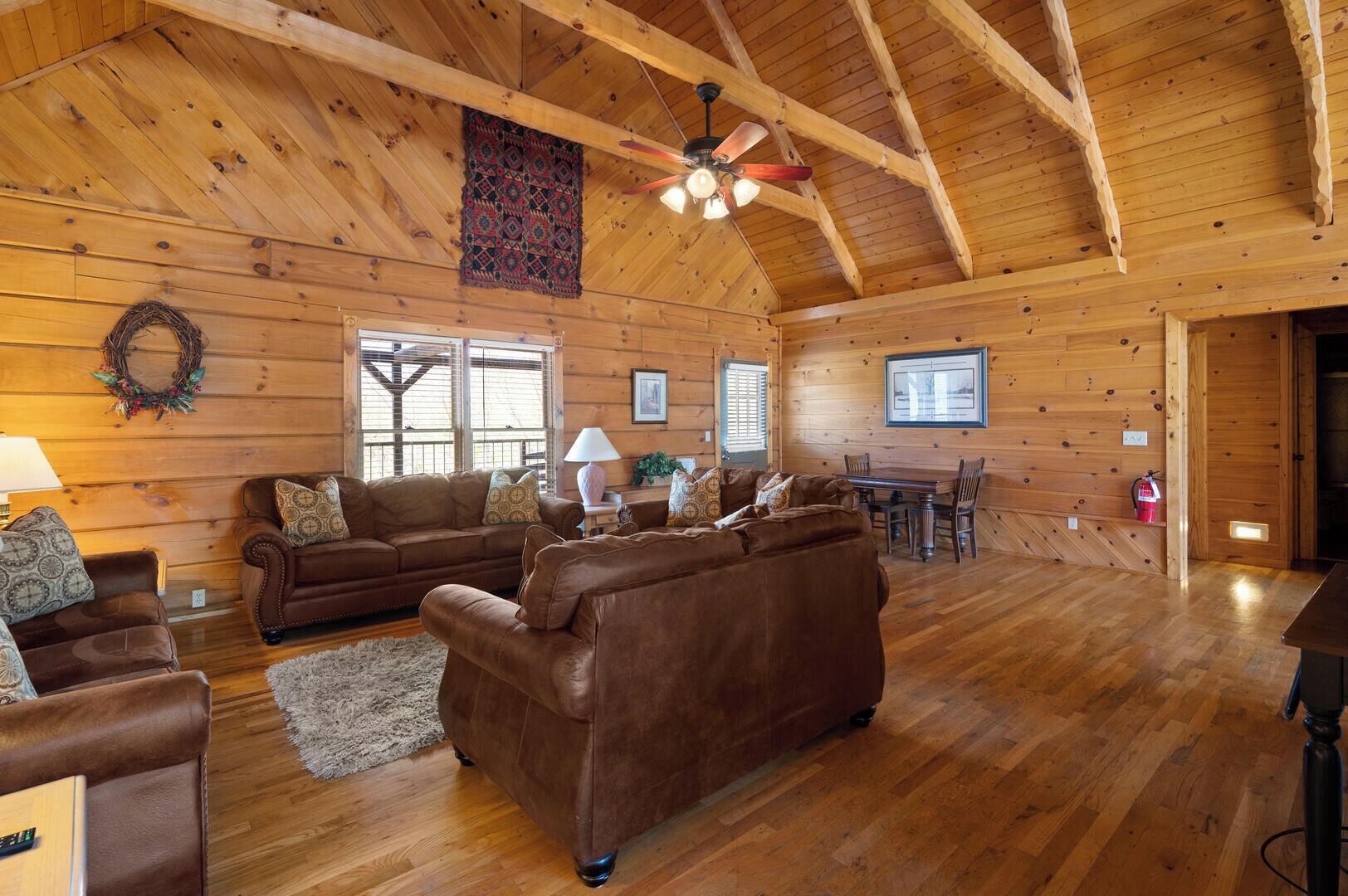A log cabin interior with a high ceiling, wooden walls, a fireplace, and a dining area.