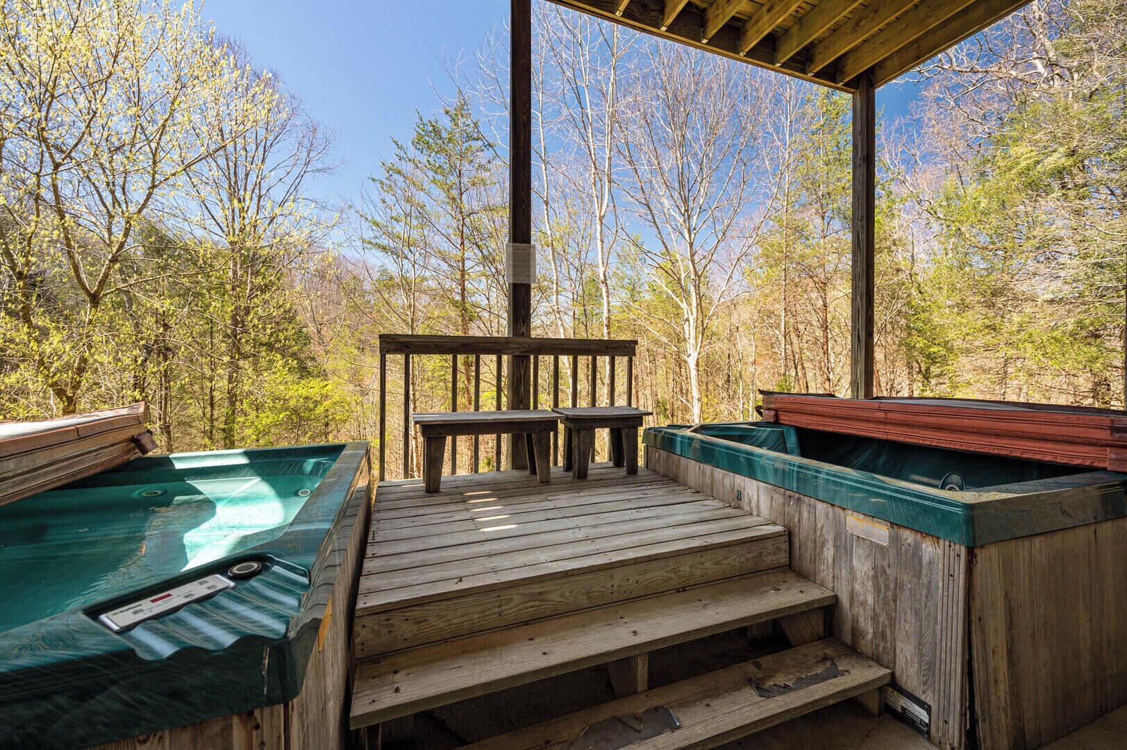 Una terraza de madera con jacuzzis y una mesa, rodeada de árboles.