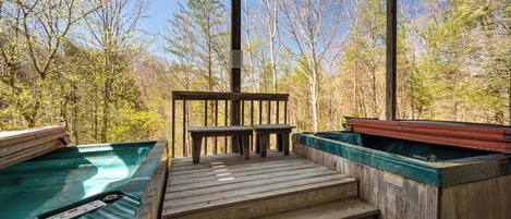 Una terraza de madera con jacuzzis y una mesa, rodeada de árboles.