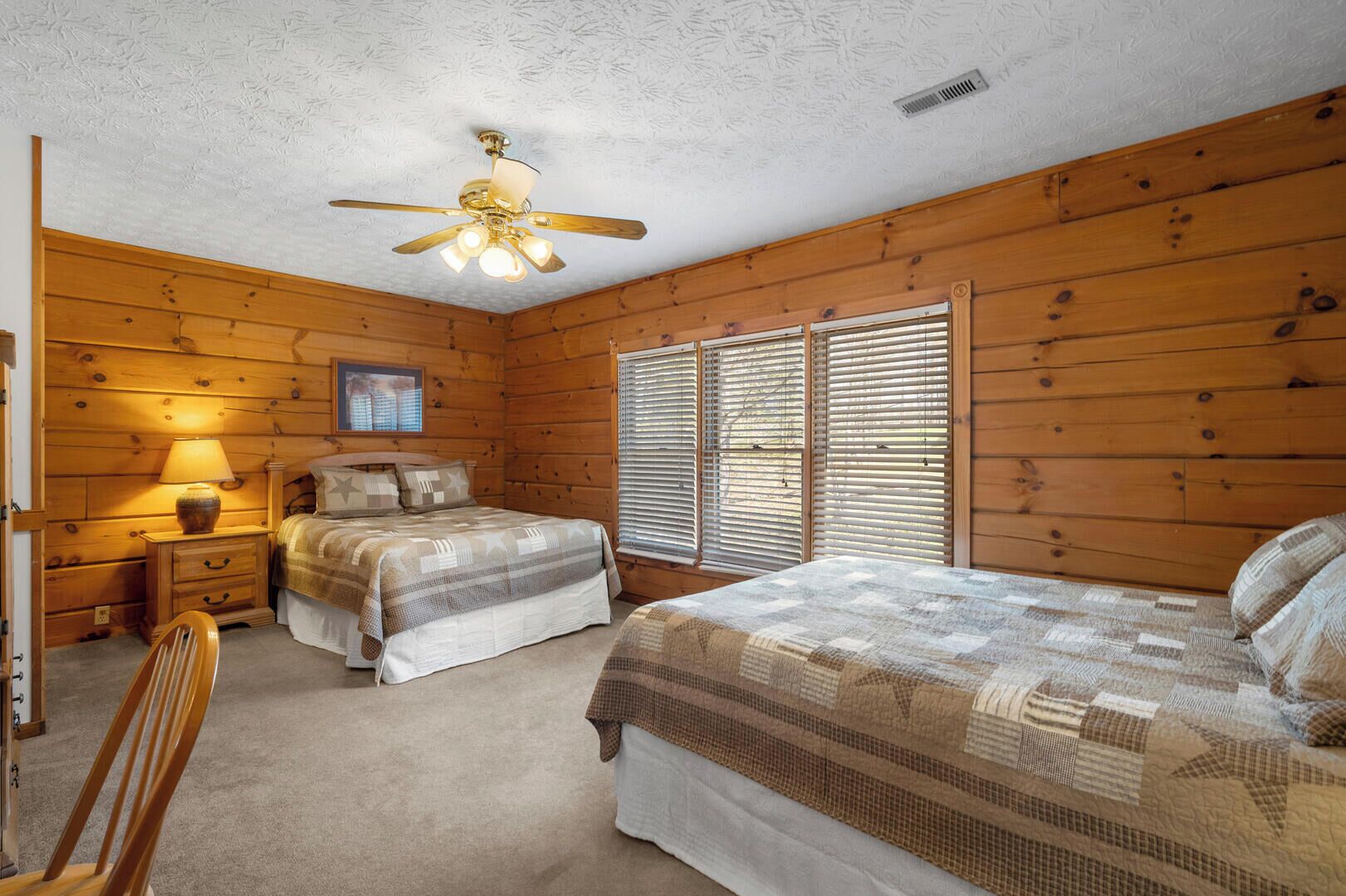 A cozy bedroom with two beds, a wooden ceiling fan, and a nightstand with a lamp.