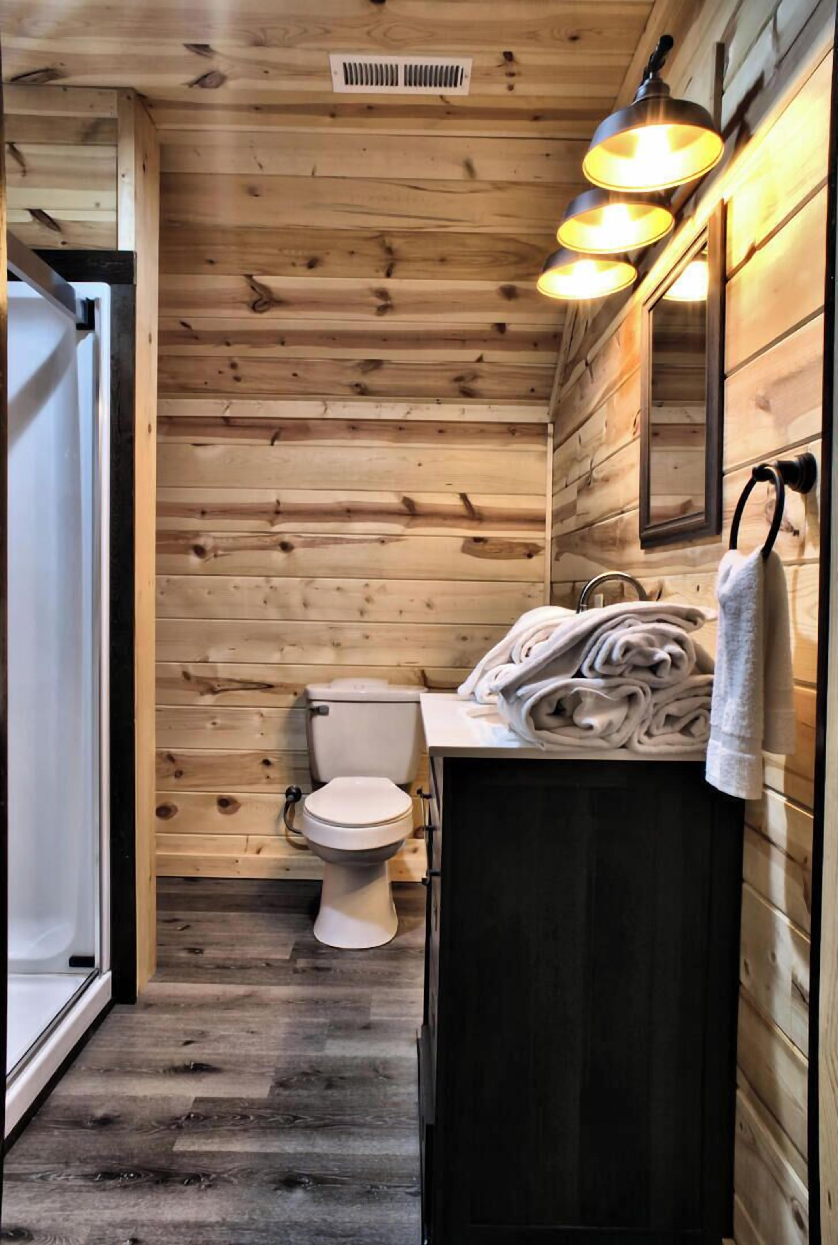 A wooden-paneled bathroom with a toilet, a sink with a towel, and a mirror.
