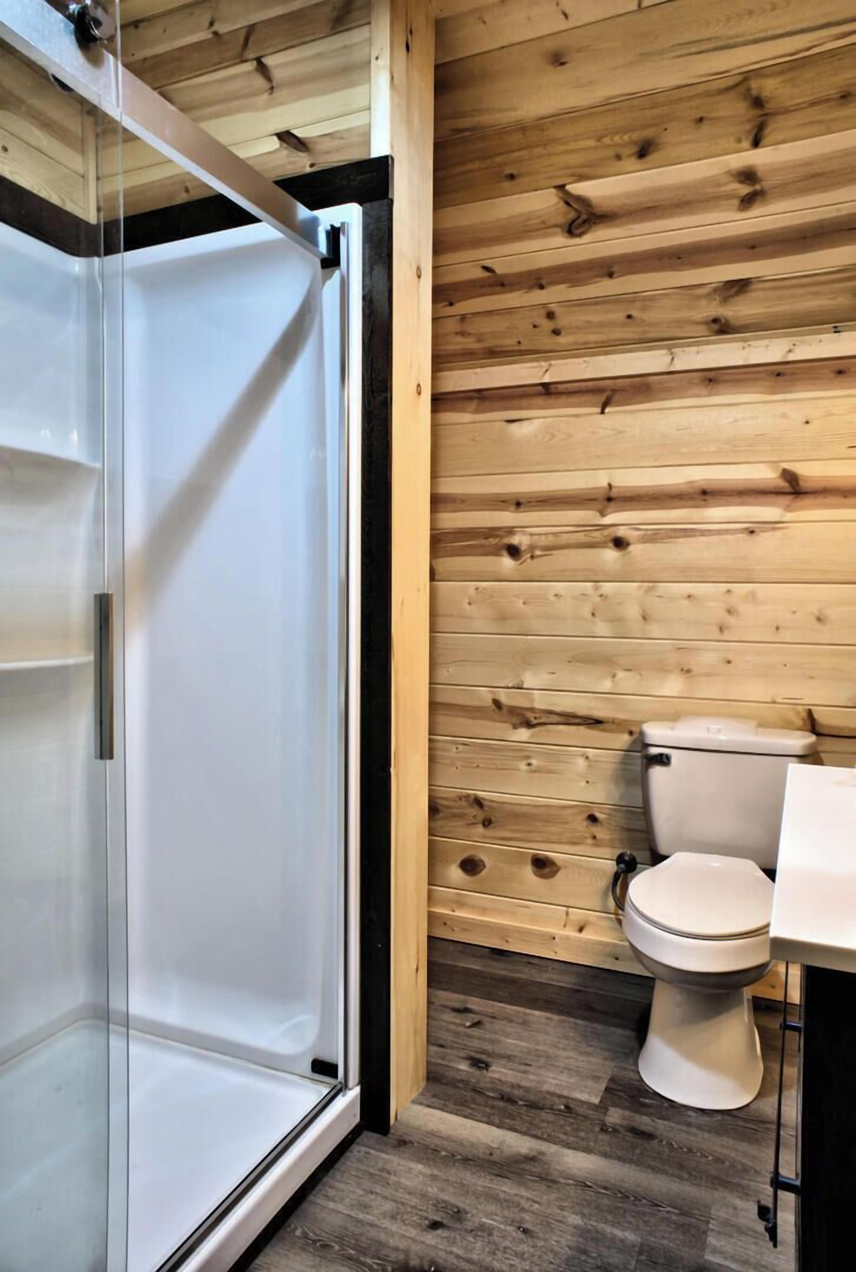 A bathroom with a wooden wall, a toilet, and a glass shower enclosure.