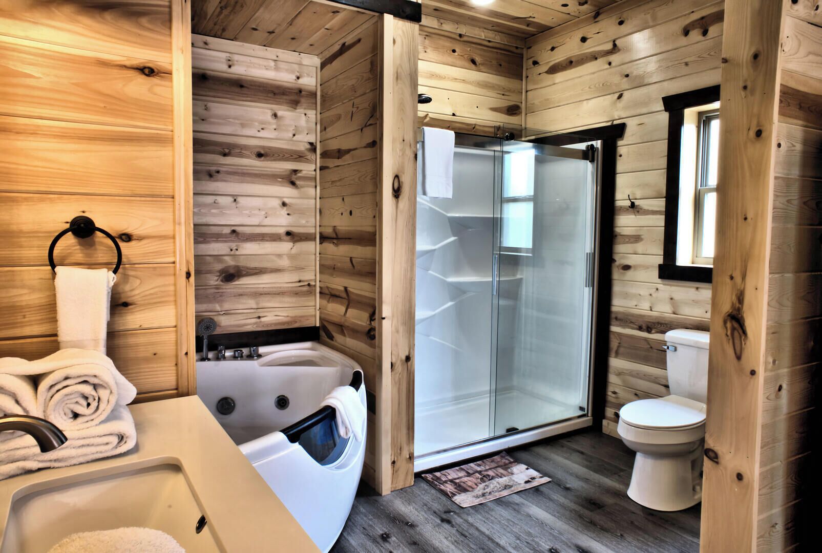 A wooden cabin bathroom with a bathtub, toilet, and glass shower enclosure.