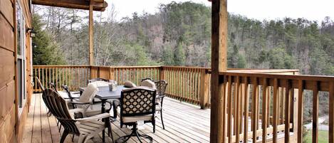 A wooden deck with a table and chairs, overlooking a forested area.