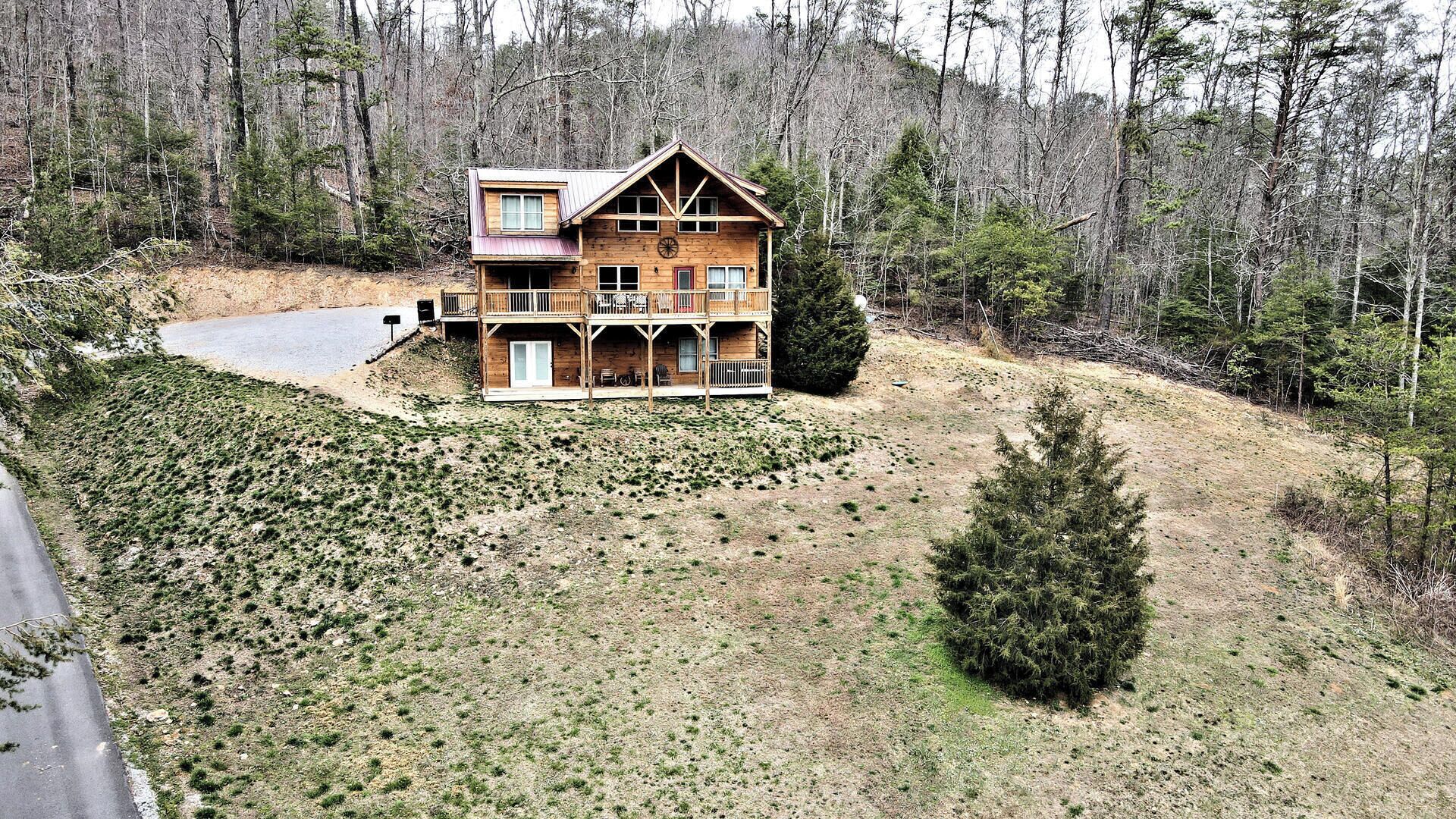 A two-story log cabin with a balcony, surrounded by a forested landscape.
