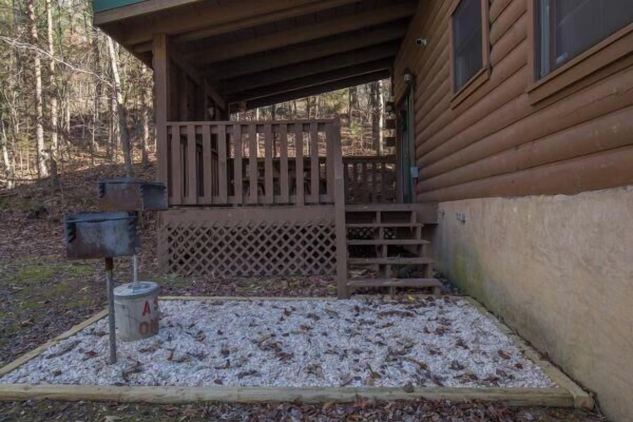 A wooden cabin with a porch, a mailbox, and a gravel area.