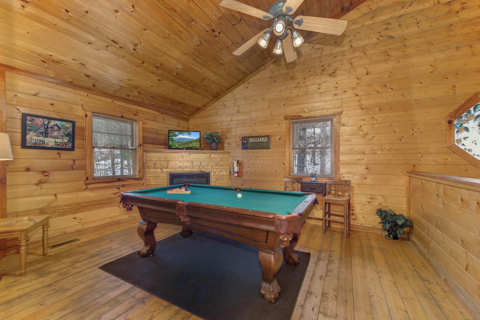 A wooden cabin with a pool table, a ceiling fan, and a fireplace.