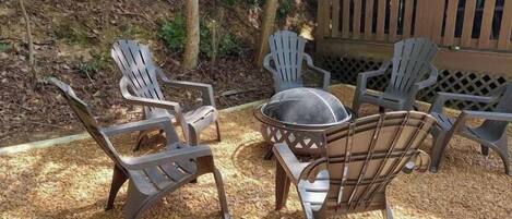 A patio area with four Adirondack chairs and a round table with a dome cover, surrounded by wood chips.