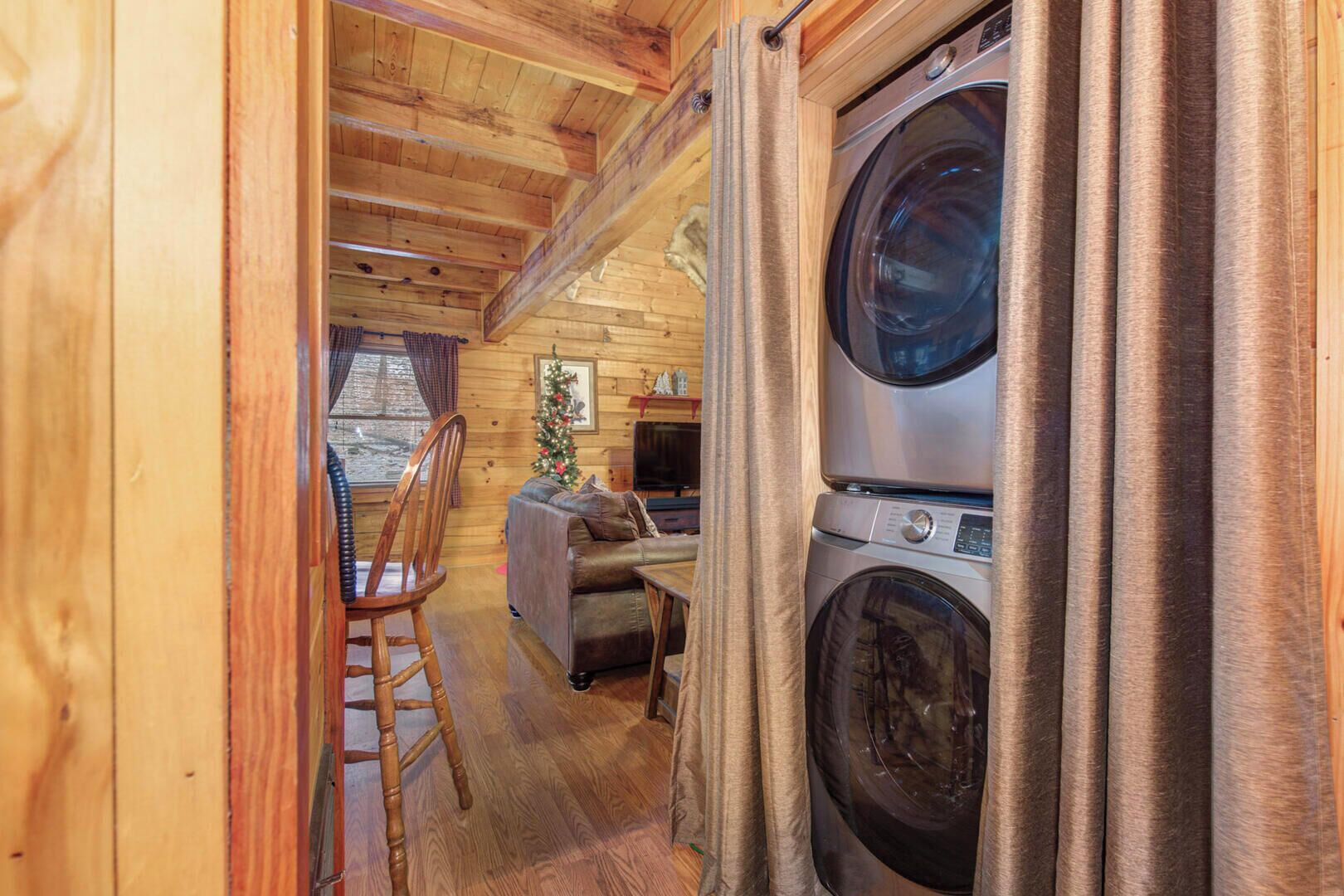 Interior acolhedor de uma cabana, com soalho de madeira, um sofá, uma poltrona e uma máquina de lavar roupa.