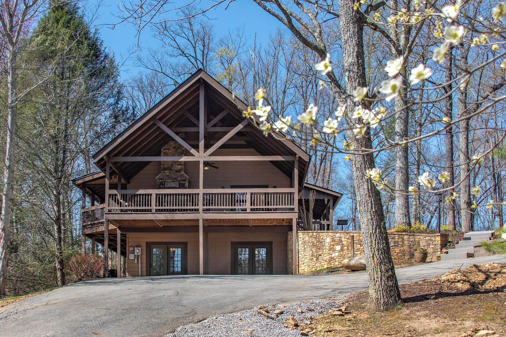A two-story lodge with a balcony, stone foundation, and a stone fireplace.