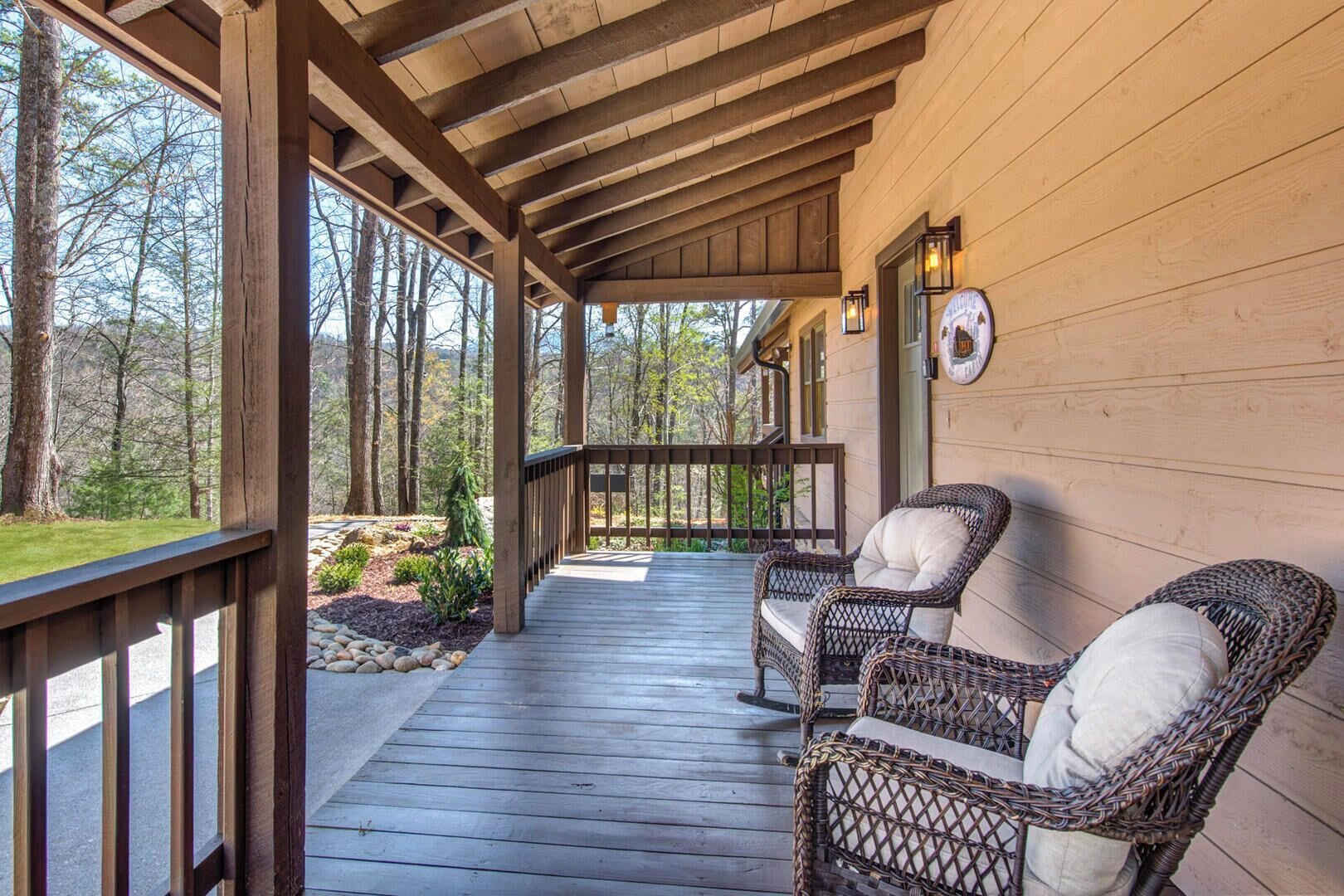 A covered porch with two wicker chairs and a stone pathway leading to a wooden deck.