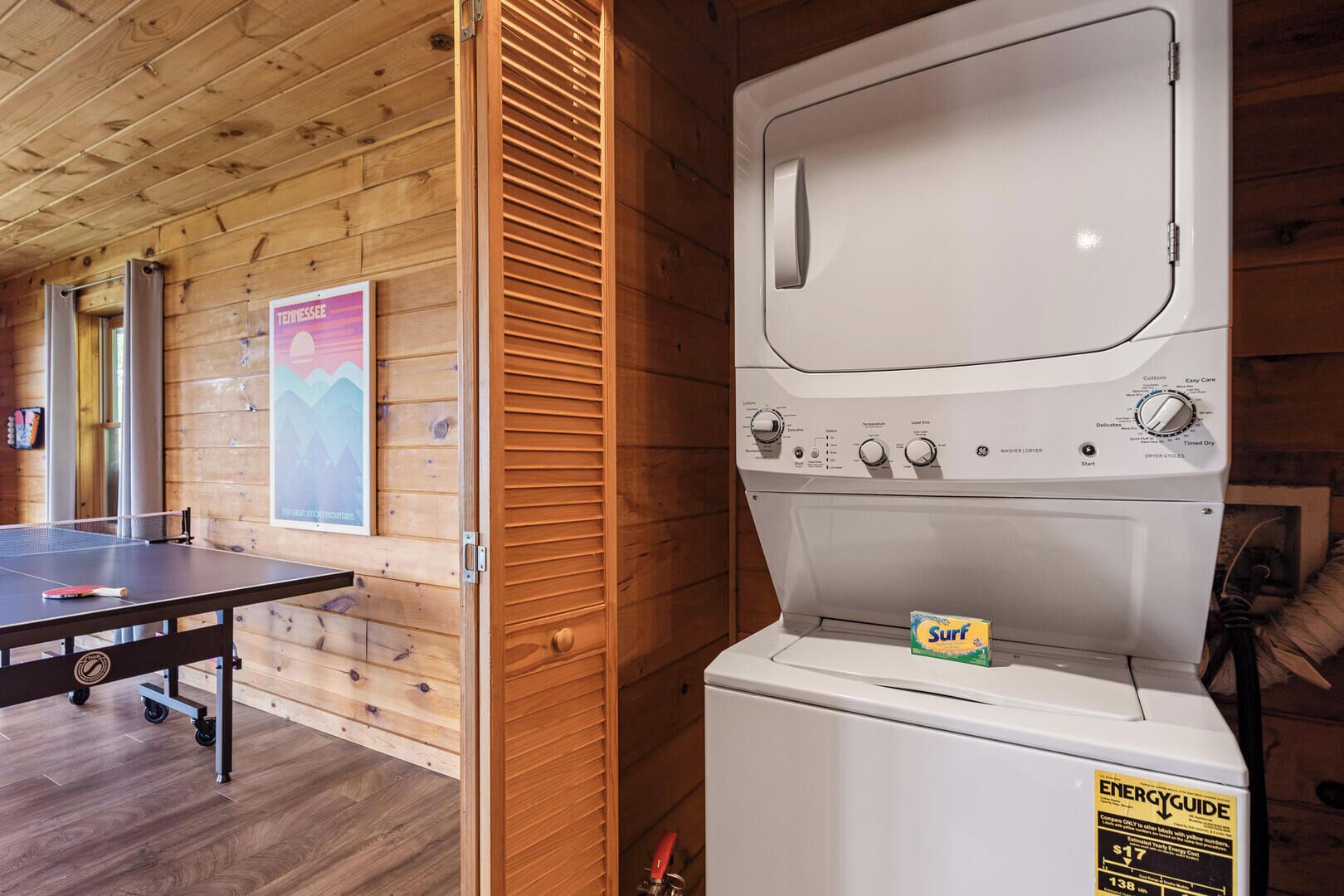 A laundry room with a front-loading washer and dryer, a ping pong table, and a poster on the wall.