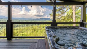 Un bain à remous sur une terrasse en bois, avec vue sur une forêt et des montagnes.