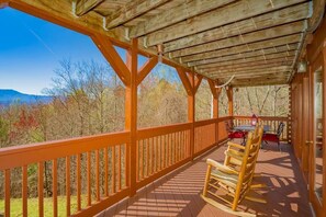 A wooden deck with a wooden chair, a table, and a view of trees and mountains. - A Mountain Dream (Sevierville)