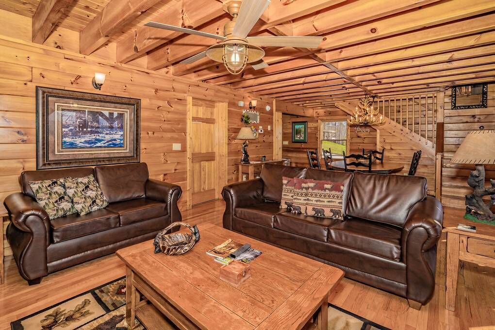 A cozy cabin interior with two leather sofas, a wooden coffee table, and a ceiling fan.