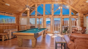 A wooden interior with a pool table, leather seating, and large windows. - A Mountain Dream (Sevierville)