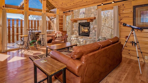A cozy cabin interior with a leather sofa, wooden tables, a fireplace, and a telescope. - A Mountain Dream (Sevierville)