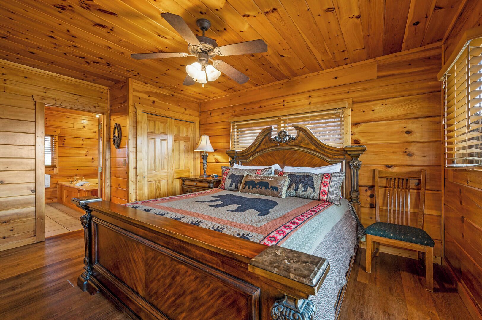 A wooden cabin bedroom with a bed, a ceiling fan, a nightstand, a chair, and a window with blinds.