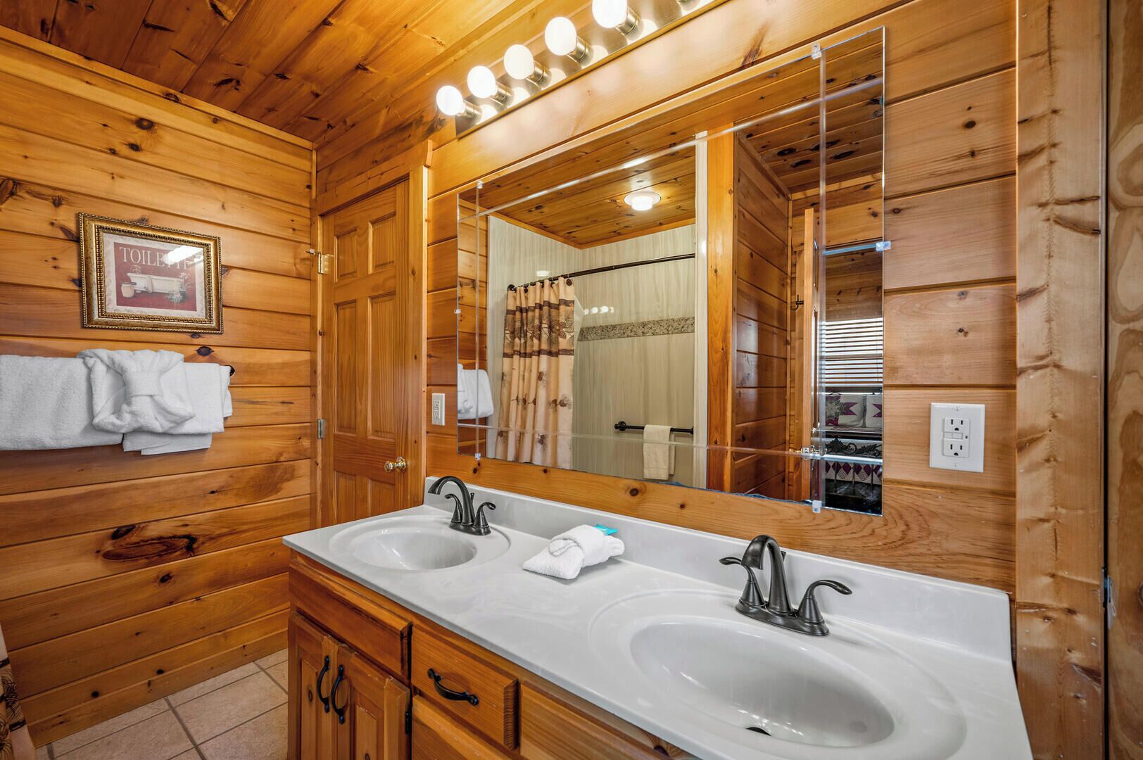 A wooden cabin bathroom with two sinks, a large mirror, and a towel rack.