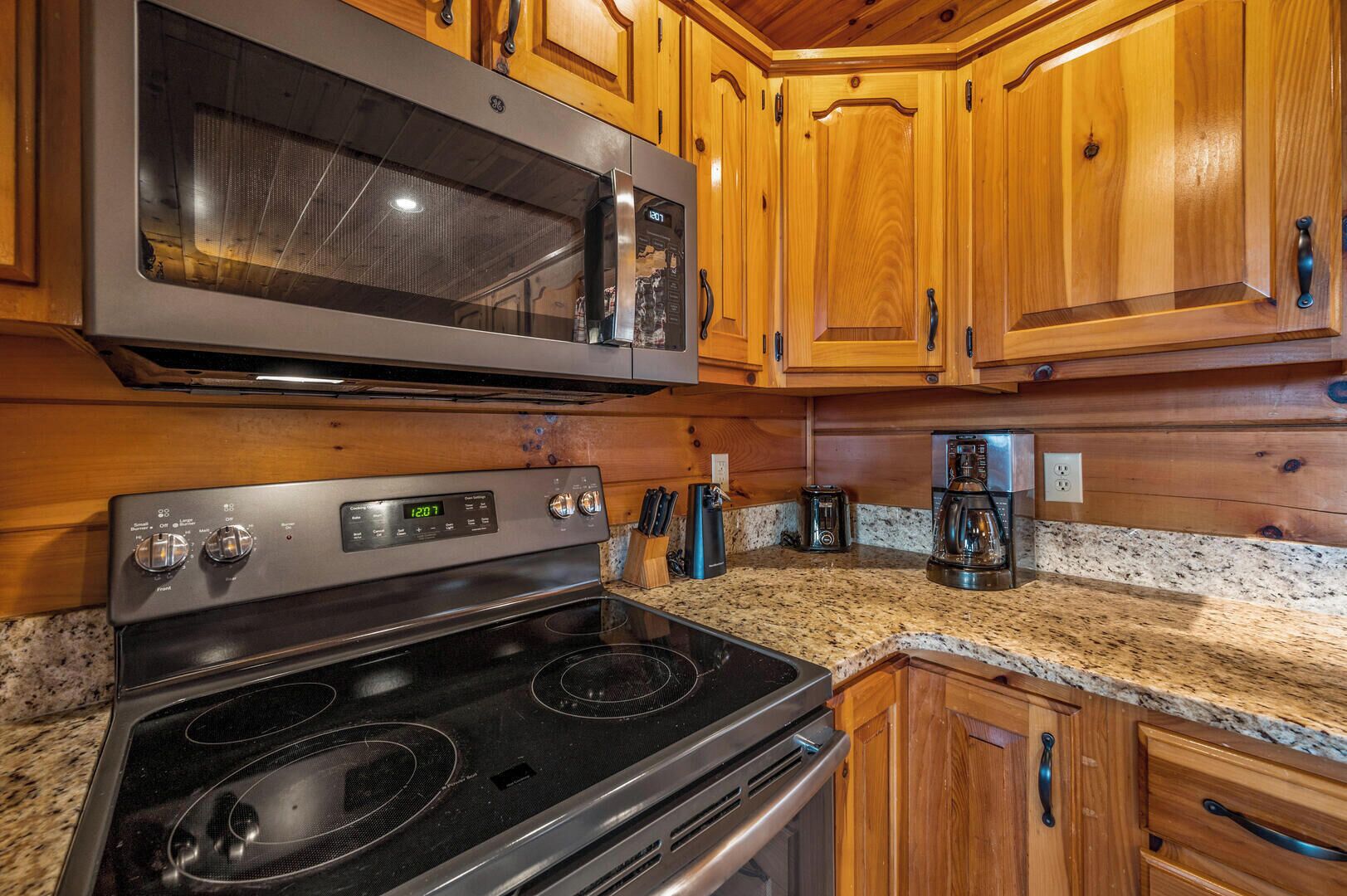 A kitchen with wooden cabinets, a stainless steel microwave, a stove, and a coffee maker.