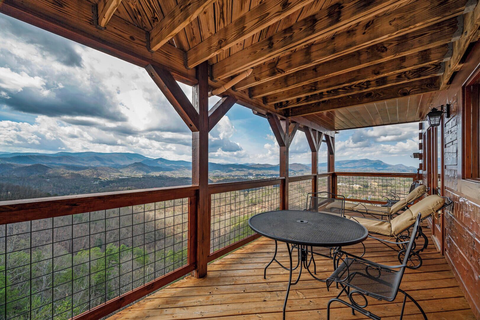Una terraza de madera con una mesa redonda y sillas, con vistas a un paisaje montañoso.
