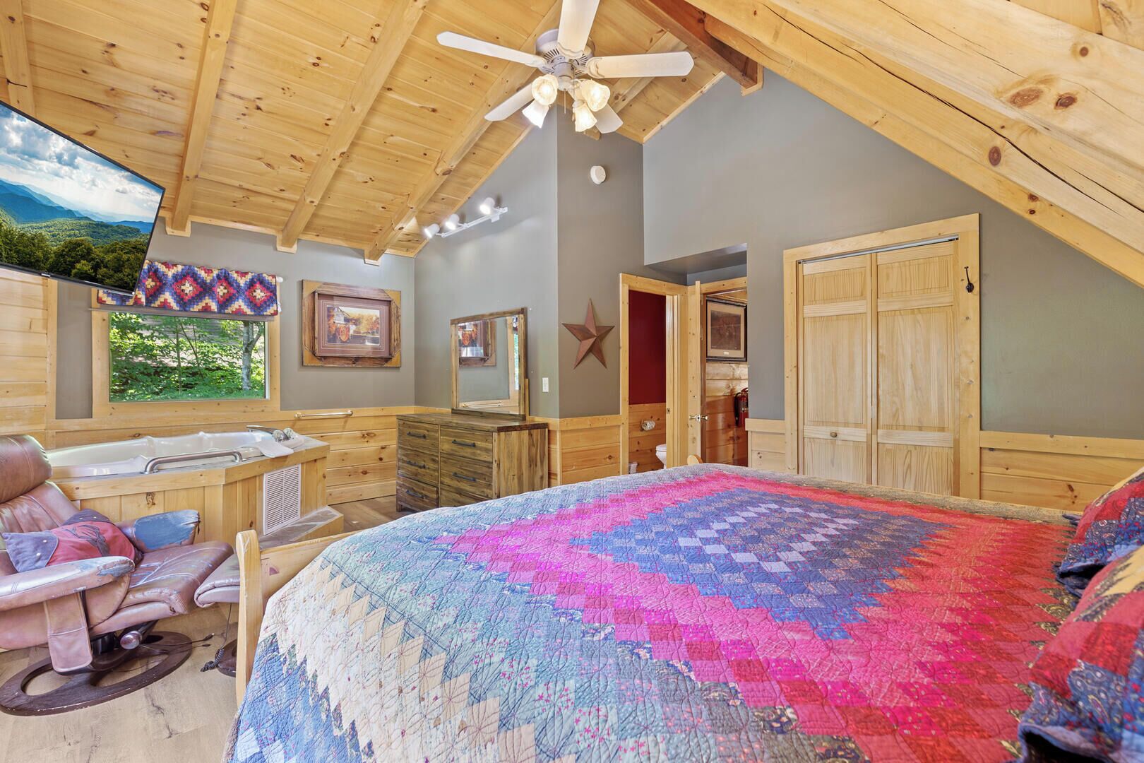 A cozy bedroom with a large bed, wooden ceiling, and a window with a view of greenery.