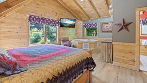 A cozy cabin bedroom with a large bed, a hot tub, and a ceiling fan. - Mountain Charm (Pigeon Forge)