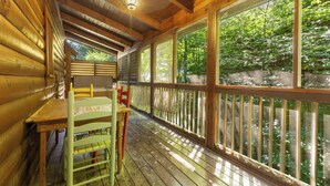 A wooden cabin with a covered porch, a table, and chairs. - Mountain Charm (Pigeon Forge)
