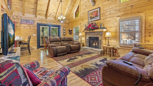 A log cabin interior with a fireplace, leather sofas, and a dining area. - Mountain Charm (Pigeon Forge)
