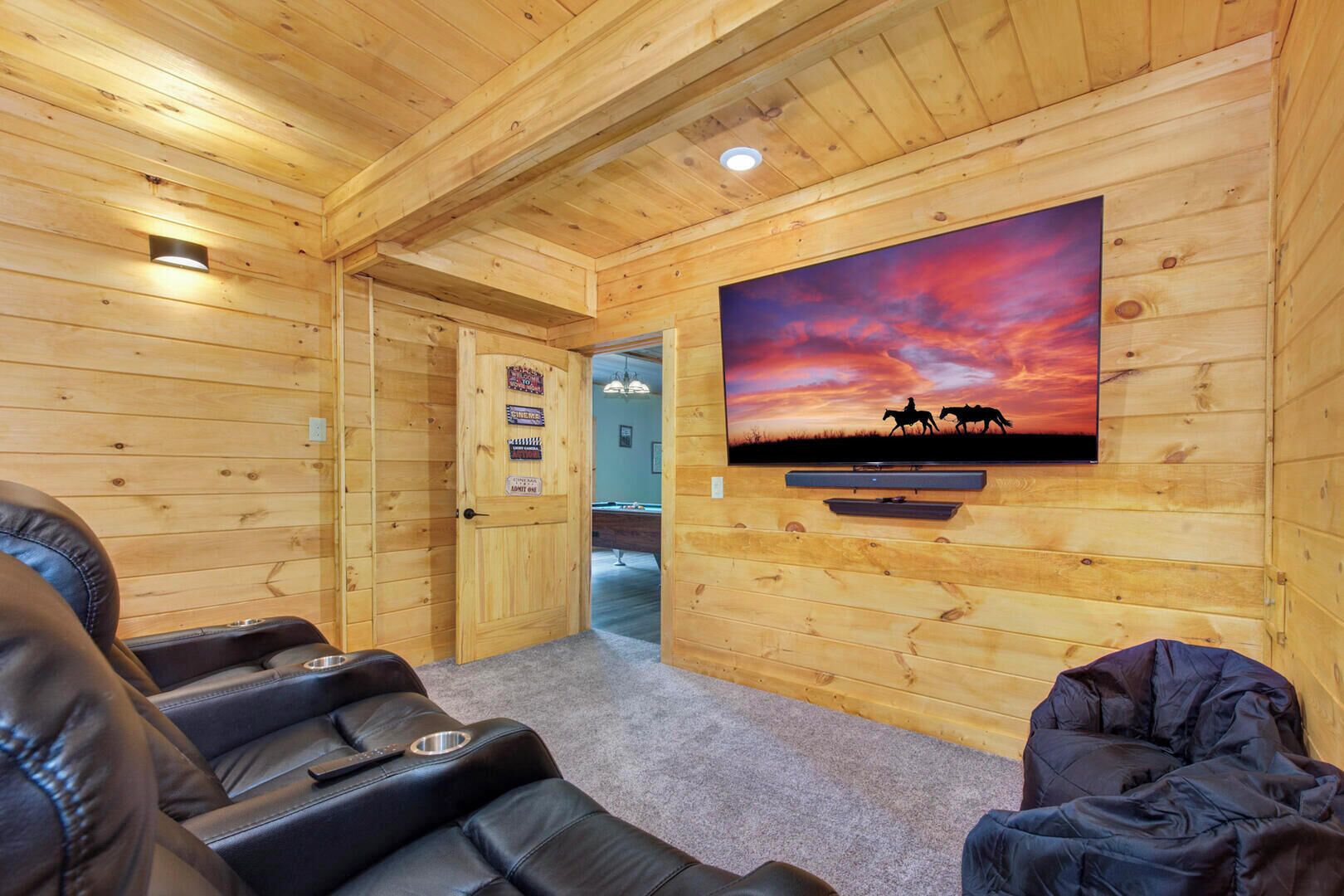 Un intérieur en bois avec un téléviseur fixé au mur diffusant une scène de coucher de soleil, des sièges en cuir et une porte donnant sur une autre pièce.