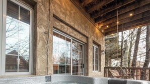 A hot tub area with large windows, wooden beams, and a view of trees and buildings.
