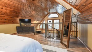 A bedroom with a large bed, a TV, a dresser, and a staircase leading to an upper level.