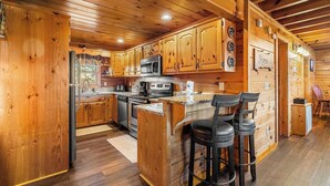 L’intérieur d’un chalet en bois comprend un coin cuisine équipé de meubles en bois, d’un four à micro-ondes, d’une cuisinière et d’un bar avec des tabourets.