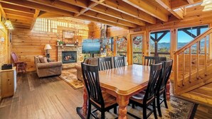 L’intérieur d’un chalet en bois comprend un coin repas, une cheminée et de grandes fenêtres donnant sur une vue imprenable sur les montagnes.
