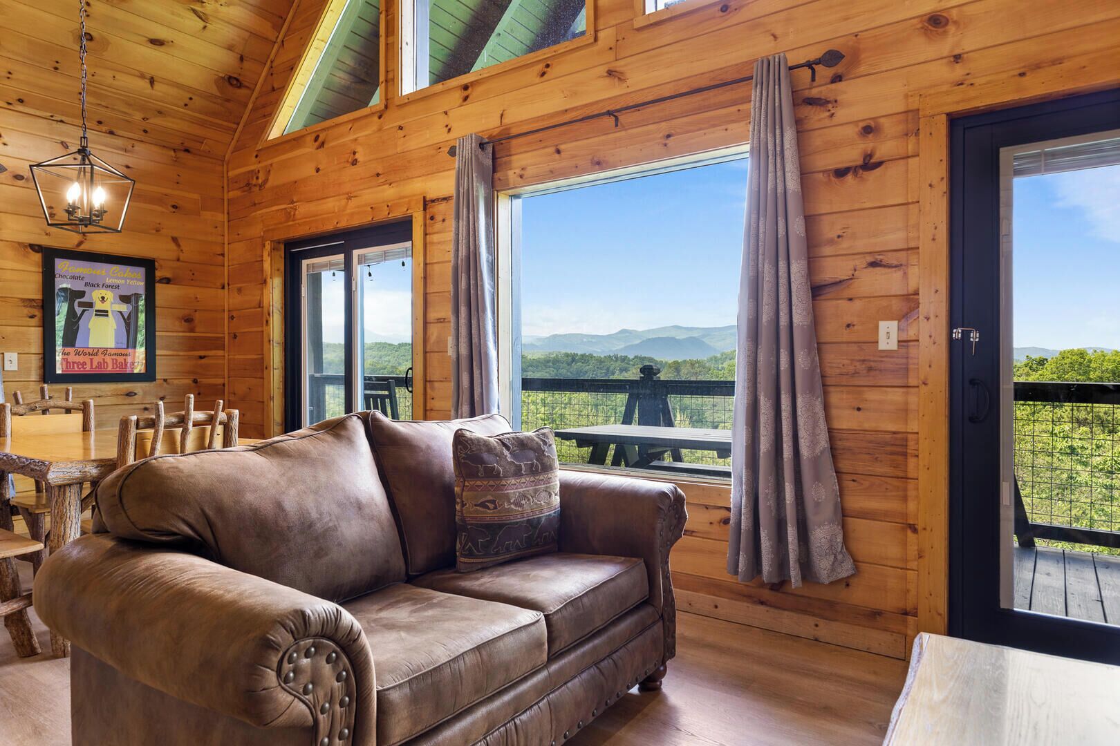 Interior acogedor de una cabaña con sofá de cuero, paredes de madera, ventanas amplias y vistas al exterior.