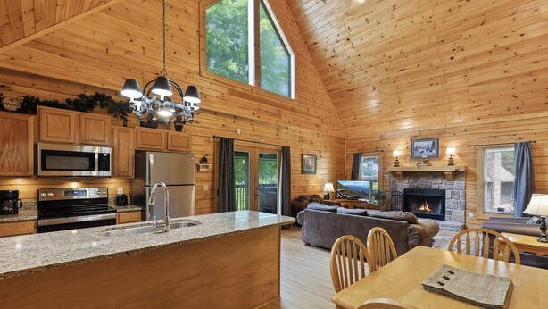 A spacious cabin with a kitchen featuring stainless steel appliances, a dining area with a wooden table and chairs, and a living room with a fireplace and a television.