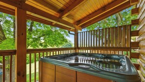A wooden hot tub in an outdoor deck area with a view of trees and a grassy yard.