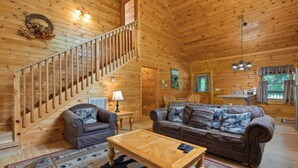 A log cabin interior with a wooden staircase, a sofa set, a coffee table, and a dining area.