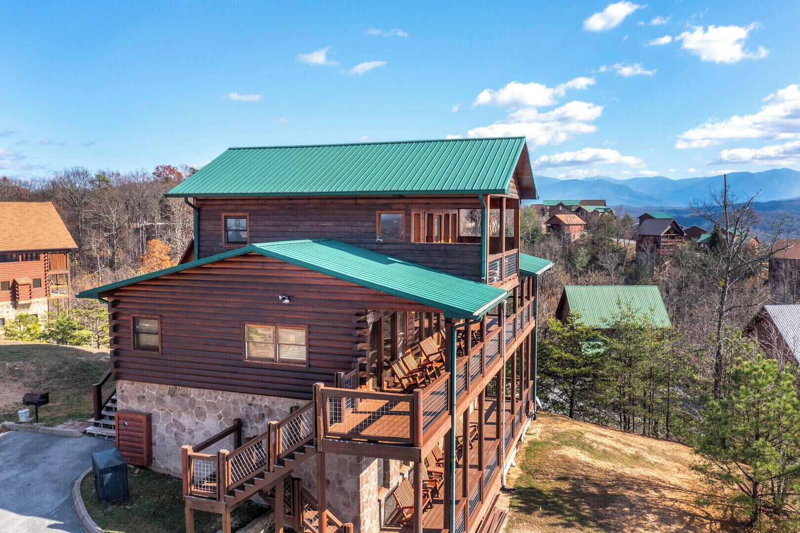 A multi-story log cabin with a green roof, a stone foundation, and a balcony with outdoor seating.