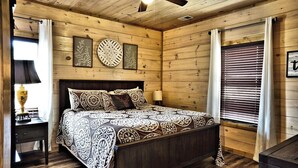 A wooden-paneled bedroom with a bed, a nightstand, a ceiling fan, and a window with blinds.