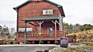 A log cabin with a porch, a small attached structure, and a fenced area with a sign.