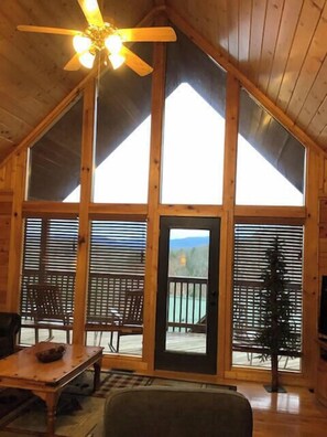 A wooden cabin with a sloped roof, large windows, a ceiling fan, and a view of a lake.