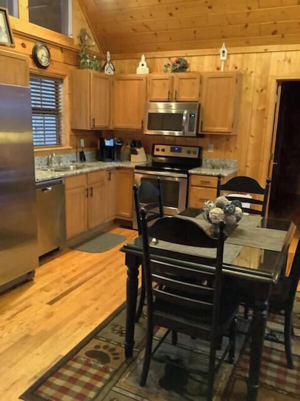 A kitchen with wooden cabinets, stainless steel appliances, a dining table with chairs, and a clock on the wall.