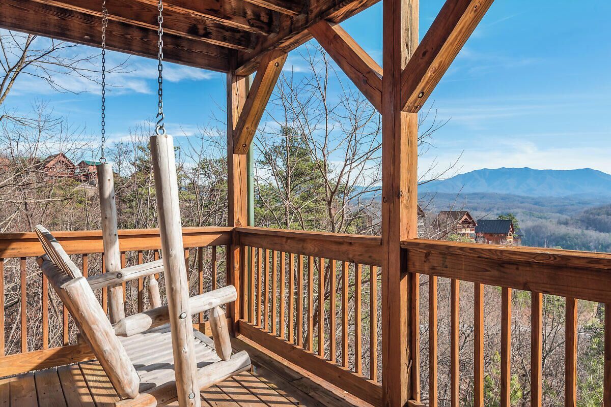 Una terraza de madera con una silla mecedora, con vistas a un paisaje montañoso.