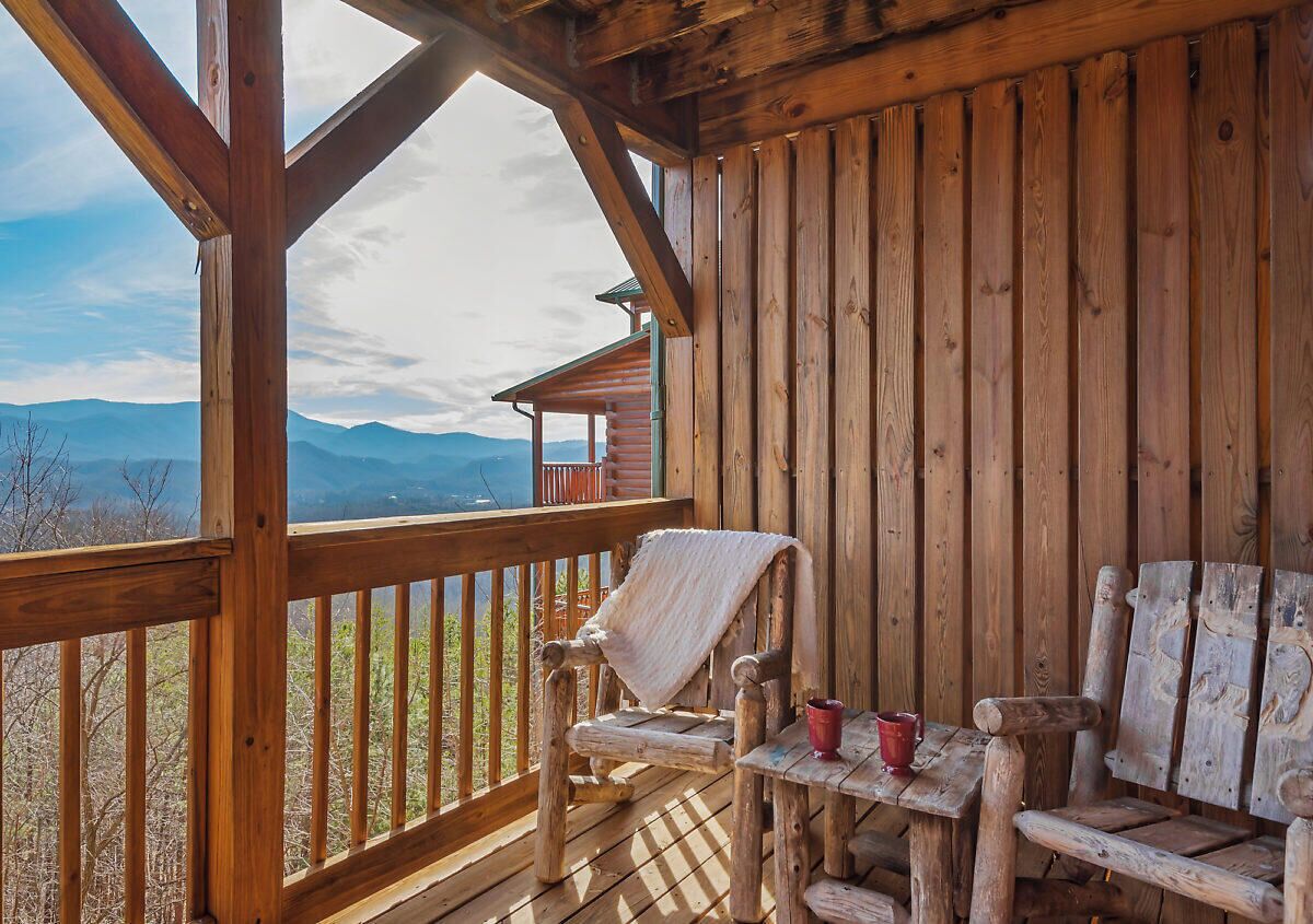 A wooden deck with a view of mountains, a covered area with a table and chairs, and a wooden railing.