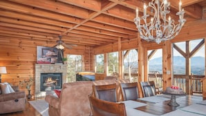 A cozy log cabin interior with a fireplace, comfortable seating, and a dining area with a view of the mountains. - Sweet Slice of Heaven (Sevierville)
