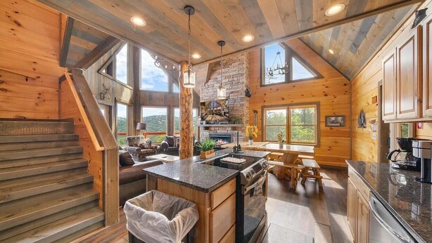 A spacious log cabin interior with a kitchen, dining area, and a staircase leading to a loft.