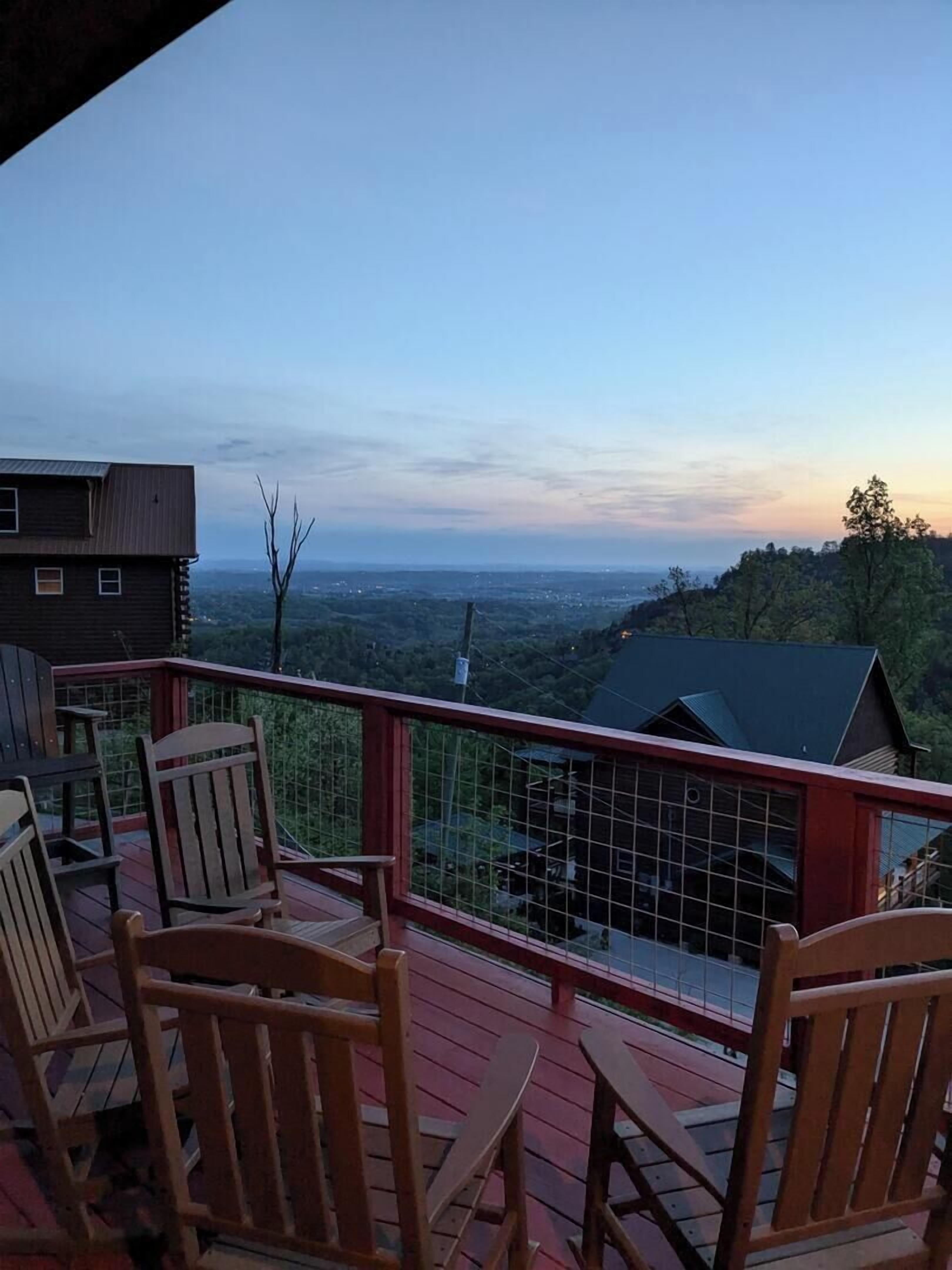 Eine Holzterrasse mit Stühlen, einer Geländer und Blick auf eine ferne Landschaft.